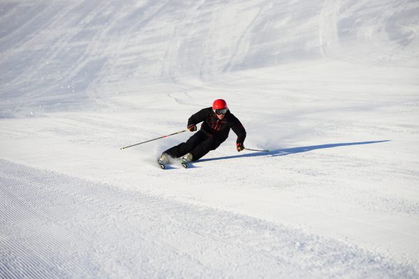 Skifahrer mit rotem Helm fährt einen Carving-Schwung auf frisch präparierter Piste