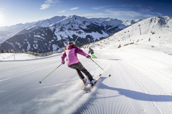 Skifahrerin in pinker Jacke auf frisch präparierter Piste vor Zillertaler Bergpanorama