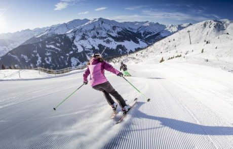 Skifahrerin in pinker Jacke auf frisch präparierter Piste vor Zillertaler Bergpanorama