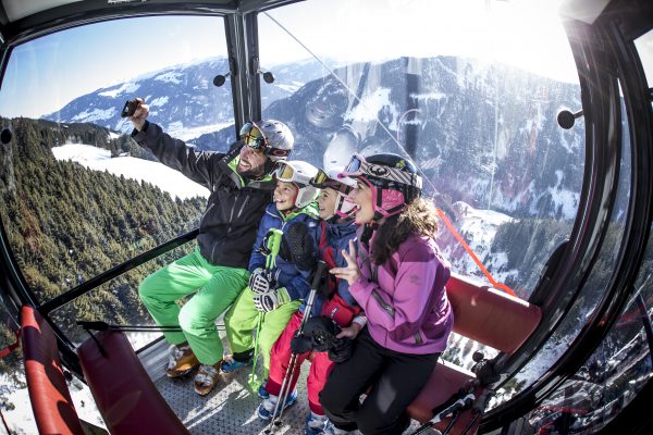 Familie mit Skihelmen macht ein Selfie in der Gondel über verschneiten Bergwäldern