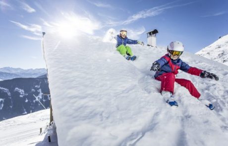 Zwei Kinder rutschen fröhlich über ein tief verschneites Hüttendach
