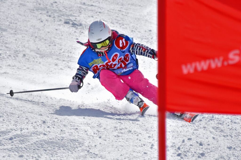 Mädchen mit Startnummer fährt beim Kinderskirennen in Hochfügen schwungvoll an einem roten Tor vorbei