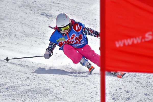 Mädchen mit Startnummer fährt beim Kinderskirennen in Hochfügen schwungvoll an einem roten Tor vorbei