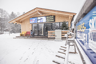 Skicheck-Hütte in Inneralpbach bei Schneefall, daneben Werbetafel